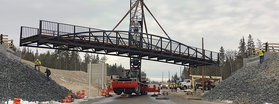 Bowstring truss trail bridge being installed over road, Un point en treillis bowstring est installé au-dessus d'une route
