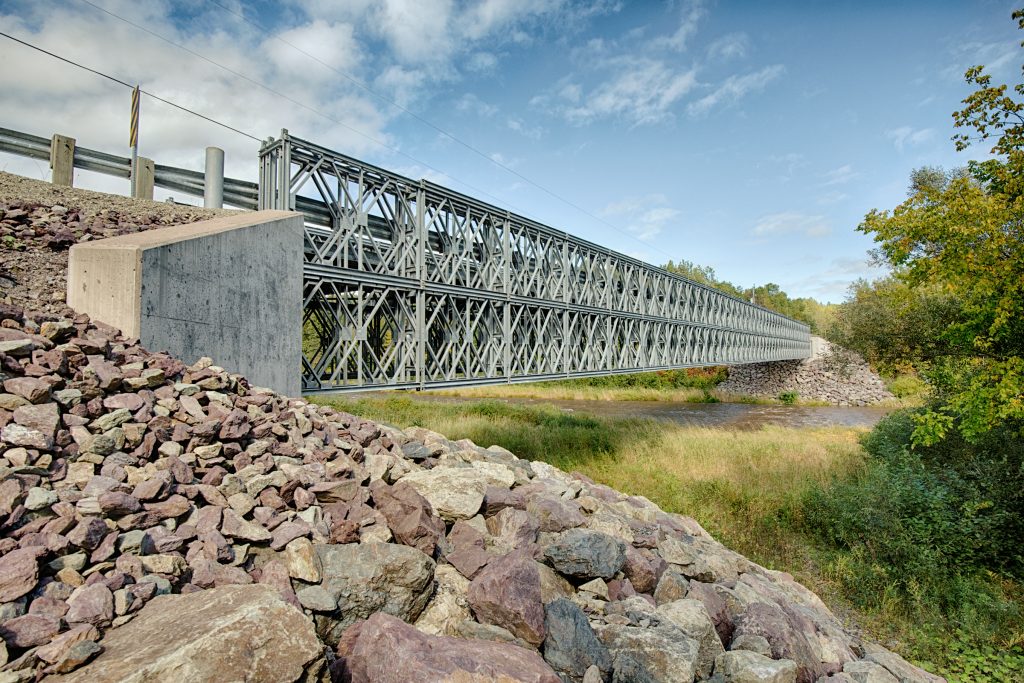 Bailey Bridge style modular panel steel bridge reaching over river, Un pont modulaire à panneaux en acier de type Bailey enjambe une rivière