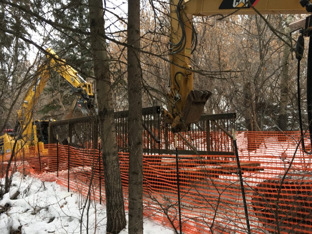 Excavators carry prefabricated bridge along trail